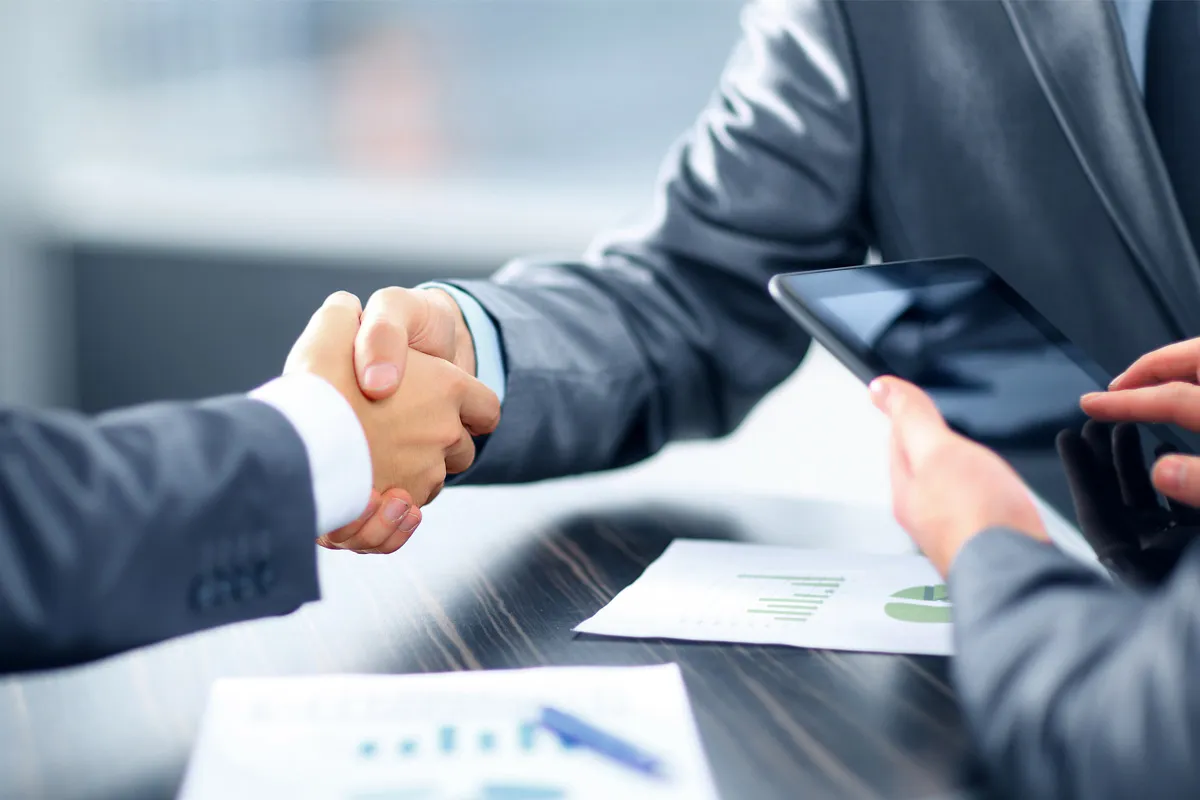 Two people shaking hands across a meeting table