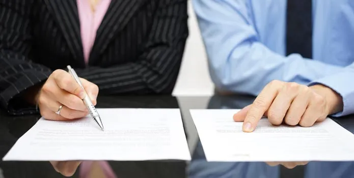 Two people signing a contract across a desk