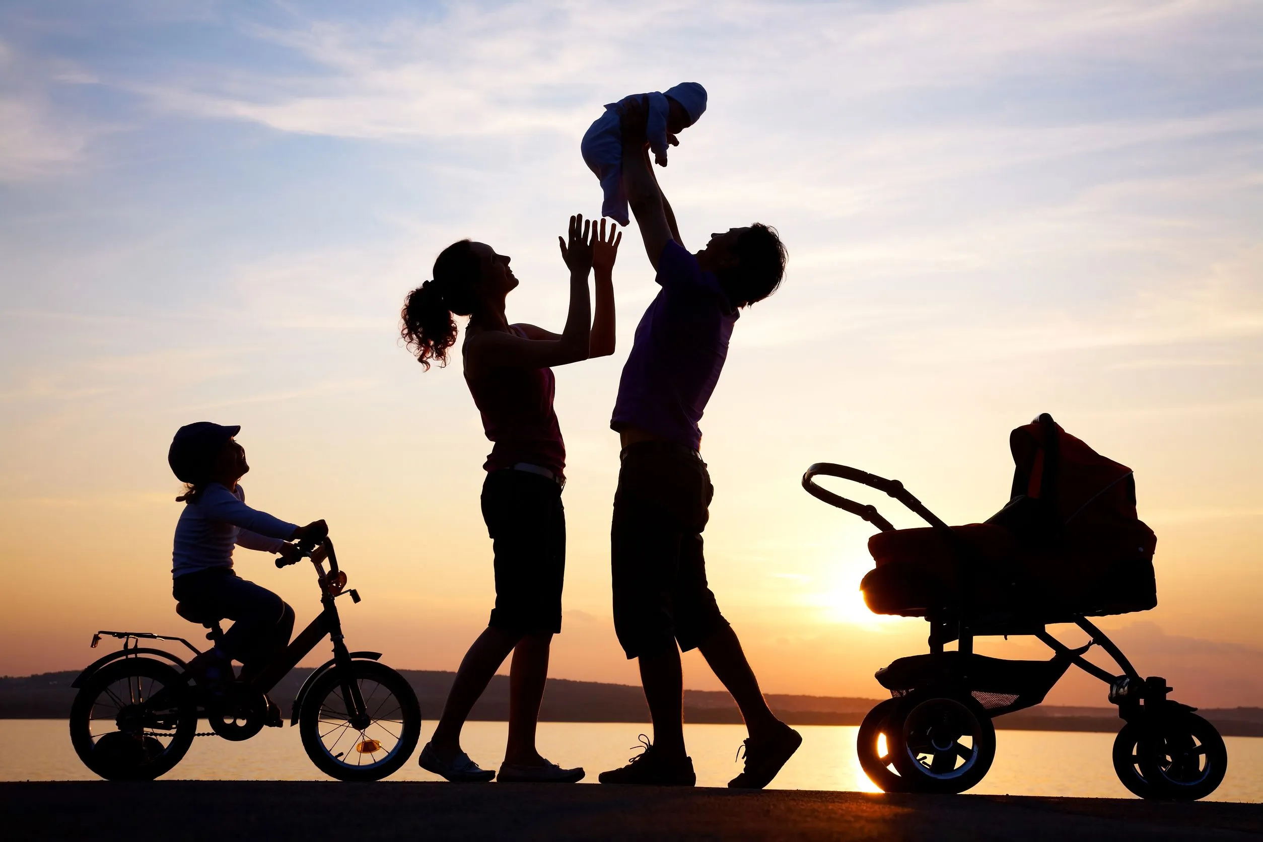 A family silhouetted against a sunset, a child lifted into the air