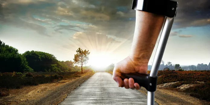 A person on crutches on an open road at sunrise